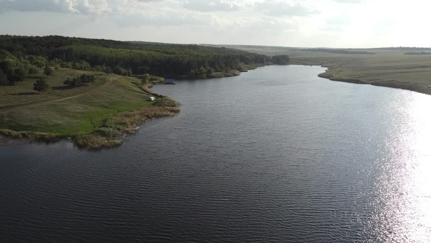 Aerial footage of a calm, dark-blue pond (reservoir) nestled in the wide, green valleys of the Donetsk region, Eastern Ukraine.