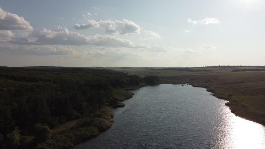 Vast rural landscape featuring a large agricultural pond and earthen dam near the village of Maloyanisol, during summer.