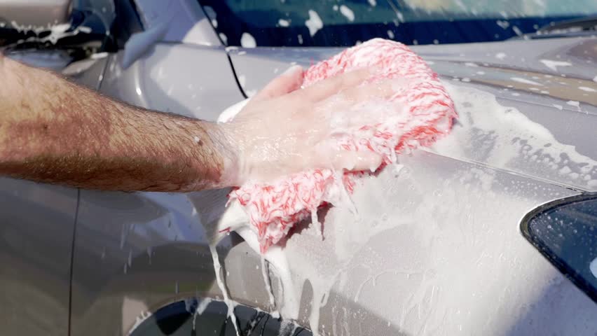 Close up cleaning grey SUV with red microfibre wash mitt and lots of suds