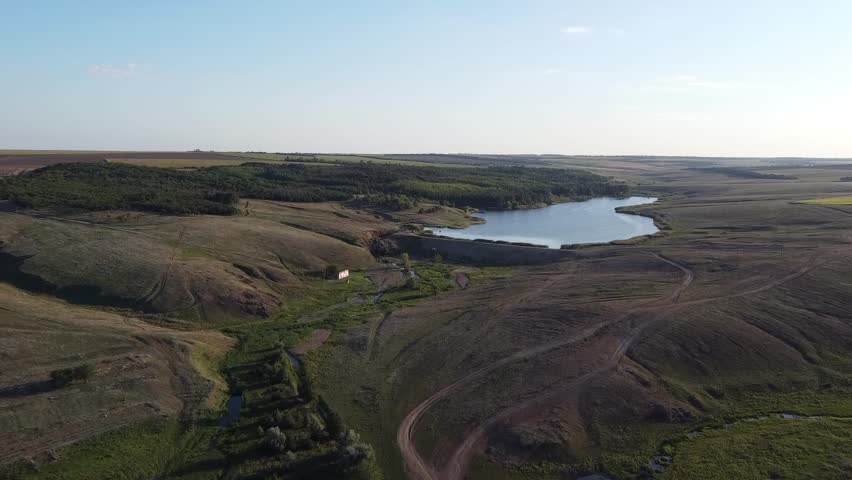Vast rural landscape featuring a large agricultural pond and earthen dam near the village of Maloyanisol, during summer.