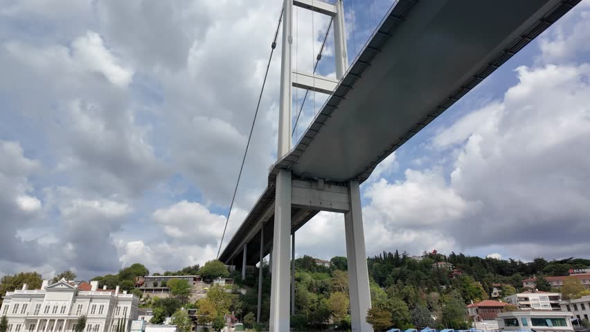 Bosphorus Bridge in Istanbul, Turkey spanning the river. Enjoy clear skies and picturesque surroundings as the camera glides smoothly beneath it, showcasing the landscape.
