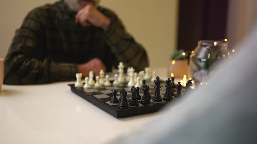Elderly woman playing chess with bearded husband at home, family leisure time