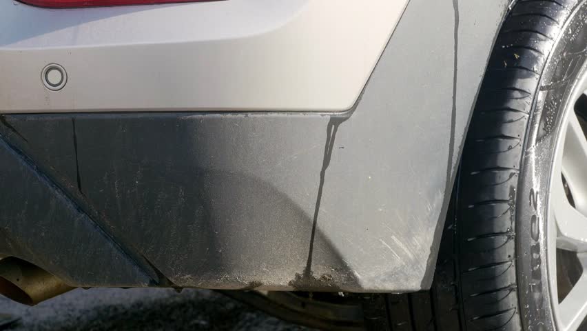 Applying cleaning product to black plastic trim on dirty rear bumper of SUV