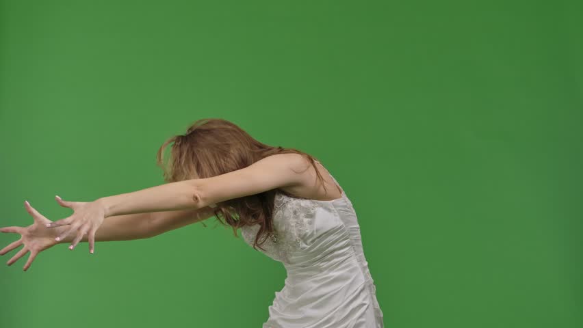 A woman dressed as a dead bride, in a white wedding dress, moves terribly like a zombie. The ghostly bride stands against a green chroma key backdrop for Halloween or spooky projects.