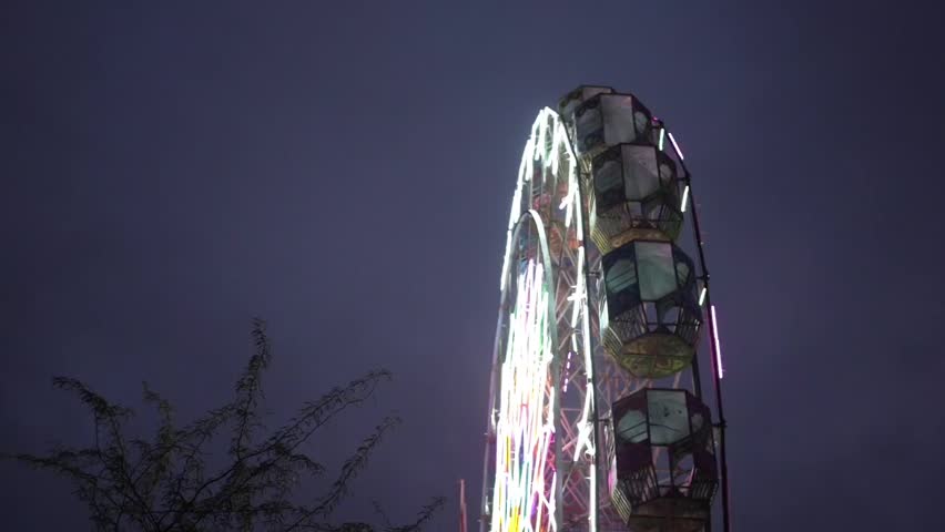 Ferris wheel lights up the night sky at an Indian fair, capturing the vibrant colors, festive spirit, and joyful atmosphere of a traditional mela.