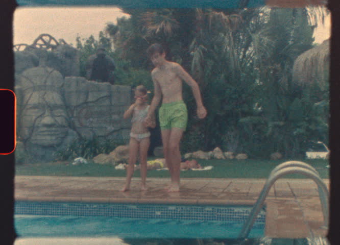 Two kids joyfully jump into a pool during a retro summer day, captured on real 8mm film with warm tones and nostalgic film grain