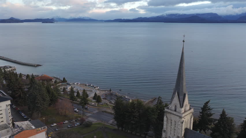 San Carlos de Bariloche city overview showing Nuestra Señora del Nahuel Huapi Cathedral by Lake Nahuel Huapi with Patagonia mountain landscape, drone pulling away