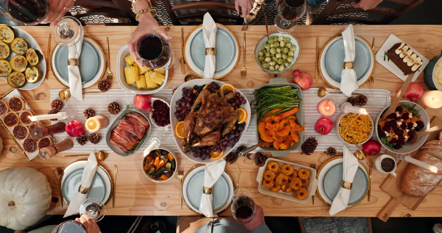 Above, hands and toast with people at dining room table together for thanksgiving celebration. Food, holiday cheers and social gathering with friends drinking red wine in home for dinner or event