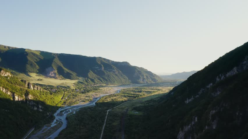 Panoramic drone view of a sunlit mountain valley, highlighting rolling hills, green meadows, and scenic landscapes, capturing the serene beauty of nature from above.