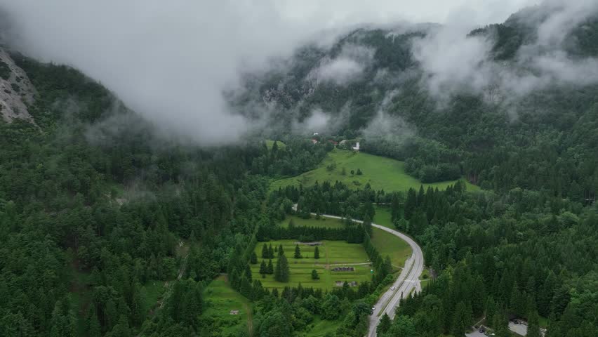 Drone aerial footage flying over alpine road in Slovenia Alps, during cloudy summer day with scenic peaceful mountains forest and natural calm atmosphere of travel