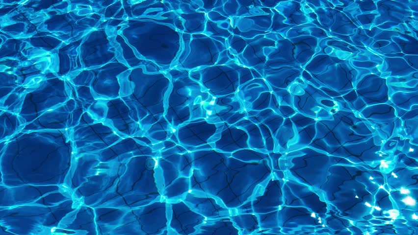 The outdoor pool area. Sunlight glares and ripples on the clear blue water.