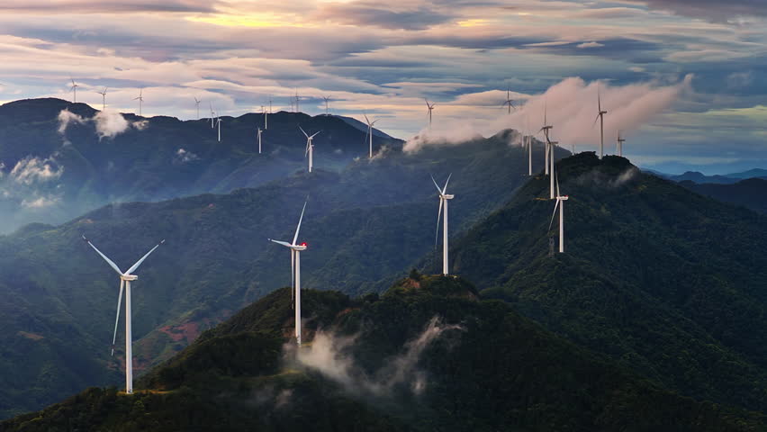 Aerial shot of wind turbines on a green mountain range generating clean renewable energy at sunrise