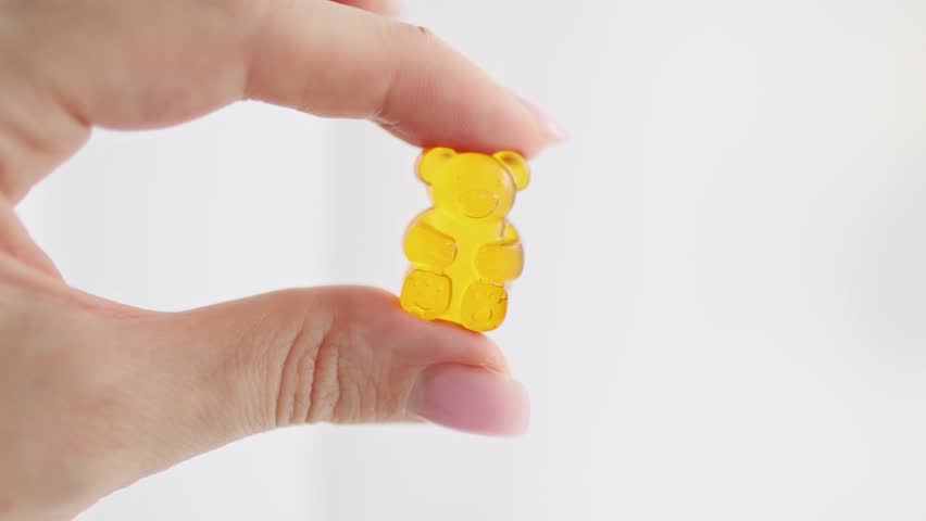 Close-up of fingers holding a soft gummy bear candy made of gelatin. Concept of CBD gummies, vitamin supplements for kids, healthy treats, and nutritional candy. Colorful chewy texture symbolizing fun