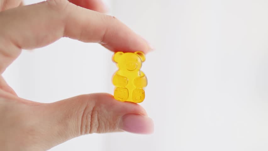 Close-up of fingers holding a soft gummy bear candy made of gelatin. Concept of CBD gummies, vitamin supplements for kids, healthy treats, and nutritional candy. Colorful chewy texture symbolizing fun