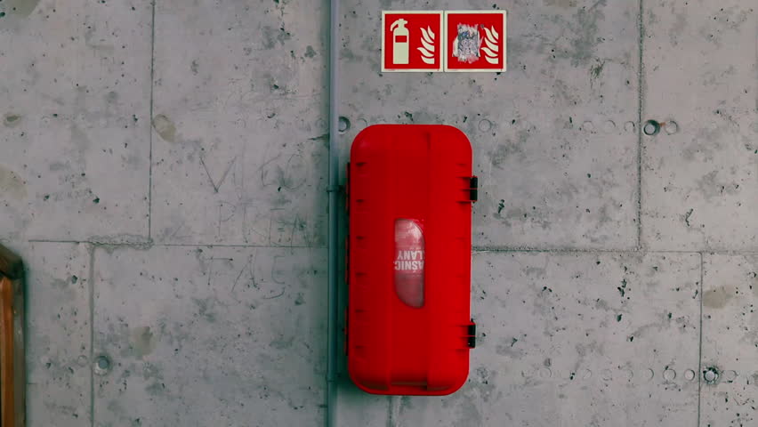 Close-up video of a red fire extinguisher inside a plastic safety case mounted on a concrete wall. Concept of industrial safety, emergency equipment, fire prevention, and workplace protection.
