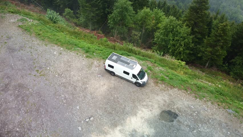 Fog over alpine forest area of southern France with a camper van parked on the edge of the mountain. The video starts pointing down over the vehicle then moves forward and pans up over the forest.