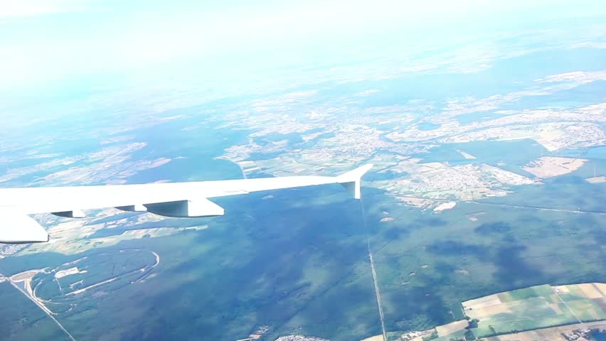 Aerial view from airplane window showcasing landscape and wing on a sunny day