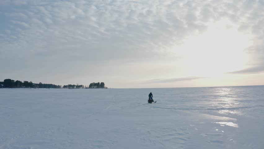 Aerial view from a drone following a man riding a snowmobile across the expanses of a frozen snowy lake. Winter extreme sports.