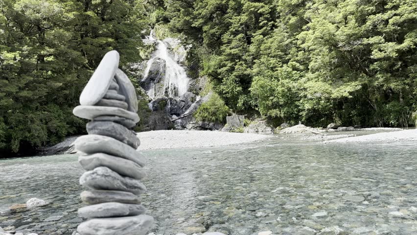 Mount Aspiring National Park, New Zealand. 1 February 2024. A hidden waterfall surrounded by stacked rocks created by travelers. filled with raw natural beauty, lush greenery, and peaceful sound.