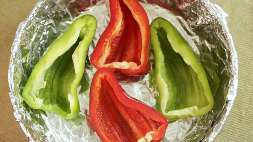 Hand drops sliced carrot over colorful pepper base, each carrot piece adding texture and depth. Bright carrot contrast with smooth pepper halves. Concept of carrot layering in vegetable preparation.