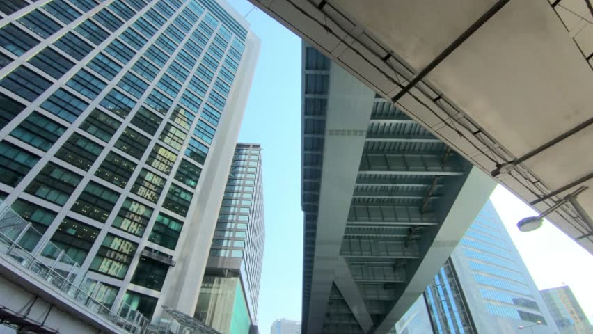 Looking up at modern skyscrapers and an elevated bridge in an urban environment