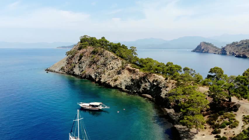 Aerial view of boats anchored near a rocky coastline with lush green vegetation
