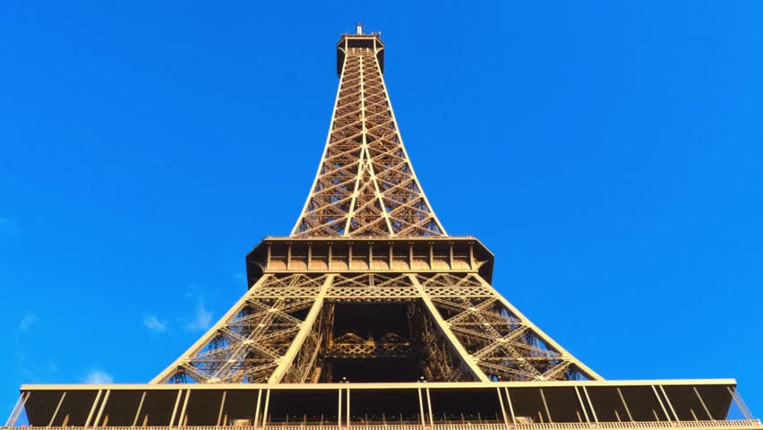 Cinematic View on Majestic Landmark Under Beautiful Sky and Summer Sunlight. From below view of majestic construction of Eiffel Tower under blue sky with clouds, Paris. Tourist attraction in summer.