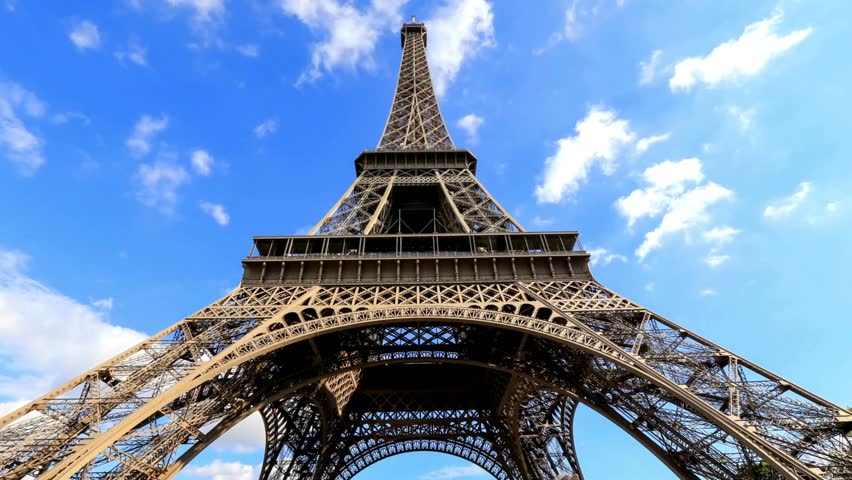 Cinematic View on Majestic Landmark Under Beautiful Sky and Summer Sunlight. From below view of majestic construction of Eiffel Tower under blue sky with clouds, Paris. Tourist attraction in summer.