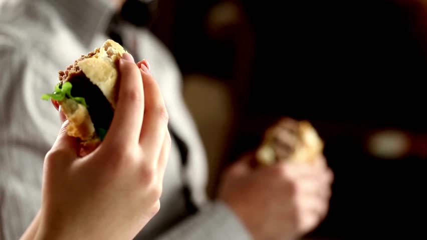 Couple eating burgers at a restaurant during date. Footage of A Happy couple eating fast food. Woman and man enjoying delicious hamburger together.