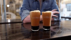 Two glasses of dark stout beer with a cascading nitro effect on a wooden table. A man in the background is waiting for the tasting - Powered by Shutterstock - Get 15% off with code: PIKWIZARD15