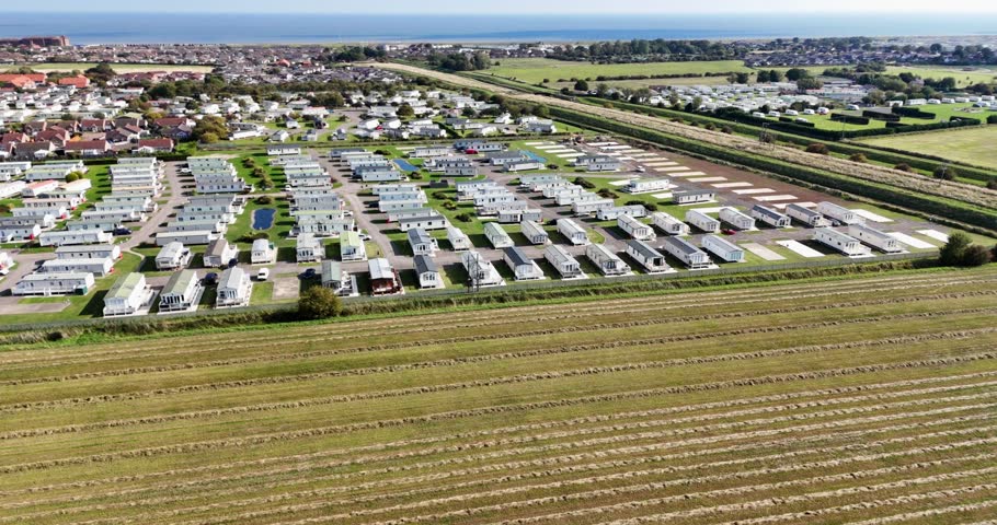 Rotating aerial view of a static caravan trailer park next to the beach with all the holiday homes set out in near rows.