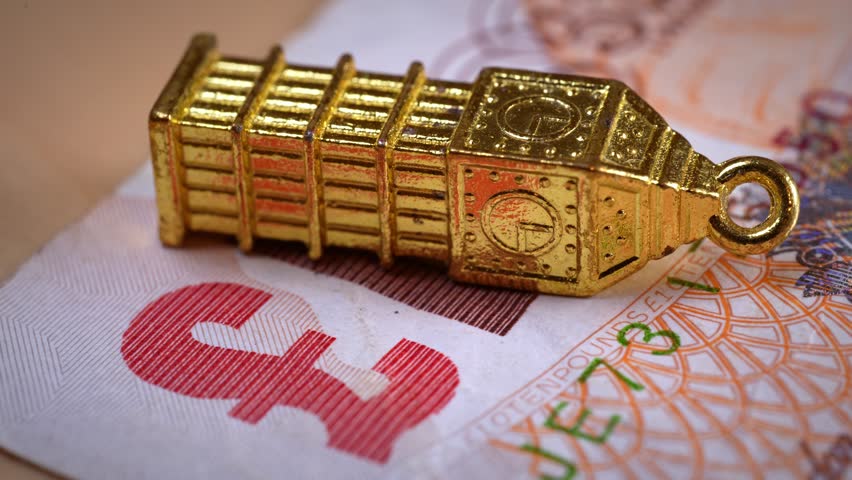 Fallen golden Big Ben miniature on a ten pounds banknote, a conceptual symbol of the UK's economic recession, inflation, fiscal imbalance, and post Brexit financial challenges in Great Britain