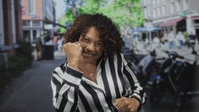 Woman clenching fists on busy city street in striped blouse with tense expression amid urban buildings and blurred cafes; strength confidence empowerment resilience. - Powered by Shutterstock - Get 15% off with code: PIKWIZARD15