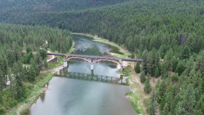 Railroad bridge over Clark Fork River in Montana. Unusual design is due to additional reinforcing structure to carry heavier trains. Wide, high shot of the bridge, river and forest.