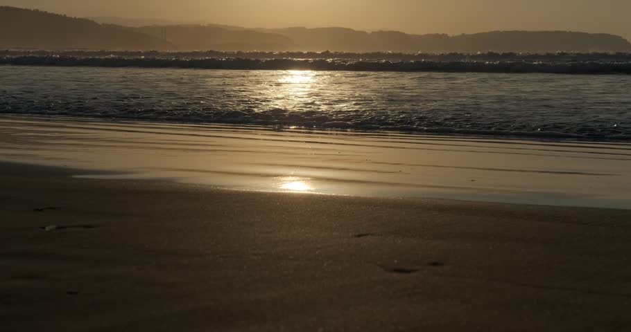 Slow motion close-up of golden sunset reflecting on ocean waves.