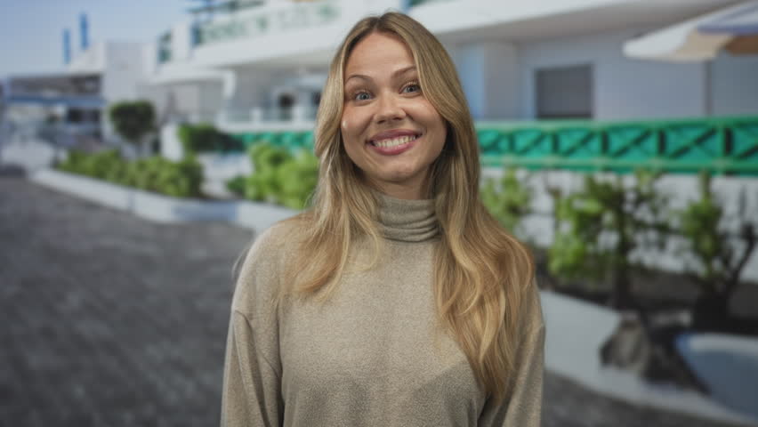 Blonde woman wearing turtleneck sweater pointing finger with smile on city street outdoors; optimism guidance joy confidence.