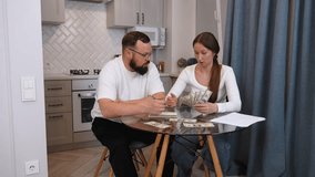 Young couple sitting at kitchen table, analyzing financial documents, calculating household expenses, sharing serious discussion about budgeting challenges, managing monetary stress together - Powered by Shutterstock - Get 15% off with code: PIKWIZARD15