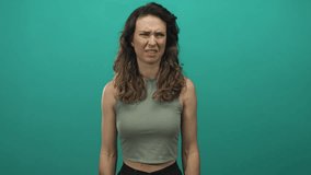 Woman with bare arms waves hand and intently cups ear as she squints and mouths words in green studio; confusion. - Powered by Shutterstock - Get 15% off with code: PIKWIZARD15