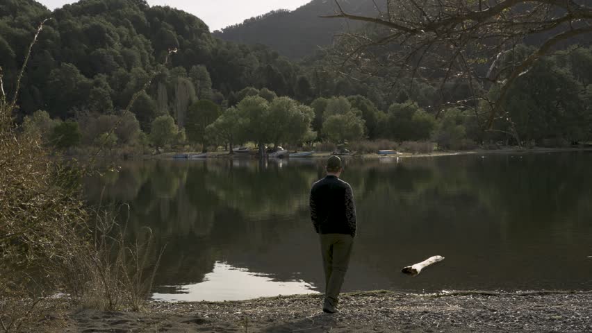 Caucasian Man Standing by Calm Lake Looking at Green Forest Reflection. Real Smooth Background Noise