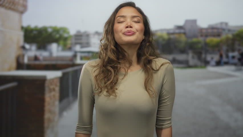 Woman enjoying peaceful moment outdoors with eyes closed in urban background, expressing happiness and relaxation on city street.