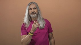Man with hand on chin in studio, long silver hair and pink shirt against peach background; thoughtful introspection curiosity. - Powered by Shutterstock - Get 15% off with code: PIKWIZARD15