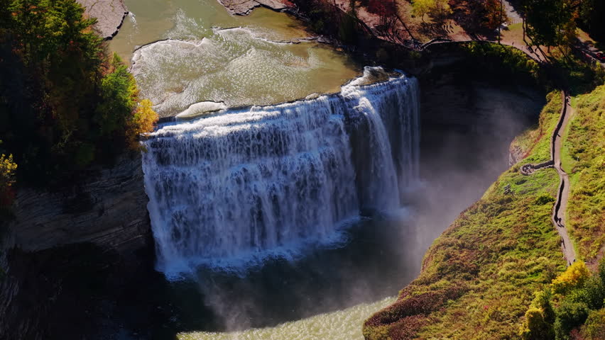 Aerial view of a powerful waterfall cascading into a deep gorge surrounded by autumn trees and rocky cliffs in Letchworth State Park, New York. High quality 4k footage