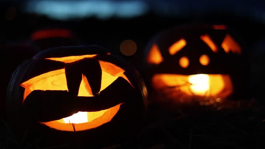 Halloween. Glowing carved Halloween pumpkins (jack-o-lanterns) with candles inside flickering in the dark night, spooky and festive autumn atmosphere, 4K ultra HD footage.