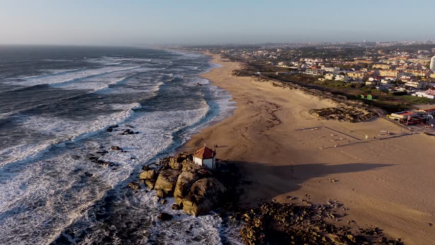 Drone rotation shot of Capela do Senhor da Pedra perched on coastal rocks at Miramar beach Portugal