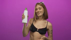 Woman smiling holds lotion bottle against vibrant pink background with short hair wearing black bikini tattoos and sunglasses showing cheerful youthful style and isolated setting. - Powered by Shutterstock - Get 15% off with code: PIKWIZARD15