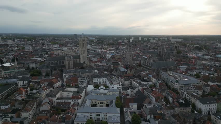 Drone footage showing the skyline of Ghent, Belgium, with the cathedral and historic buildings under a cloudy sky.