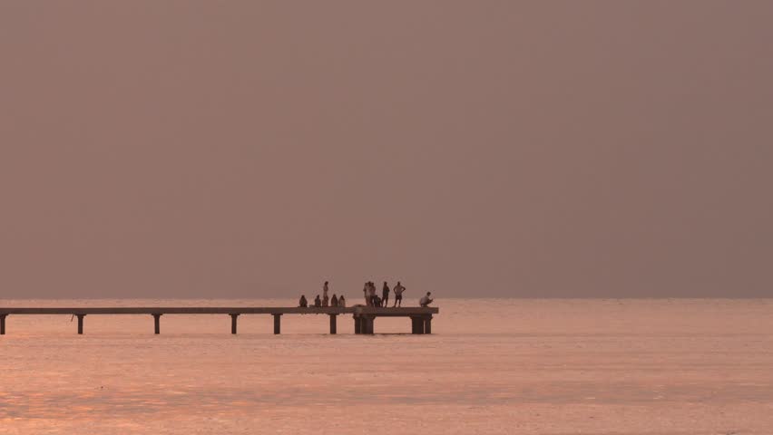 Silhouettes of group of people at pier at ocean coastline during sunset time.Maldives