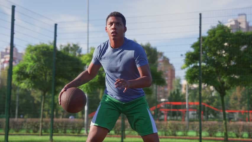 Portrait of concentrated motivated sporty fit black man basketball player practicing streetball game, performing ball dribbles skills during sports training on outdoor court.
