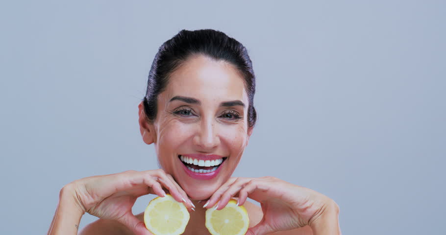 Happy woman, face and lemon in studio for skincare, glow and mockup space for results on background. Mature person, smile and pride with organic citrus fruit, beauty and vitamin c benefits in Spain