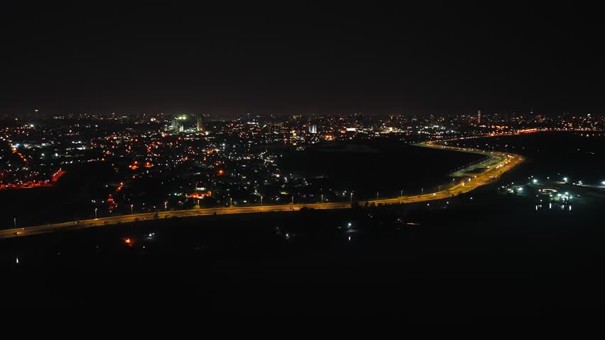 A sweeping aerial nightscape of Asuncion, Paraguay showcasing the illuminated city skyline and Costanera avenue from Heroes of Chaco bridge under a starry sky, captured in high definition.